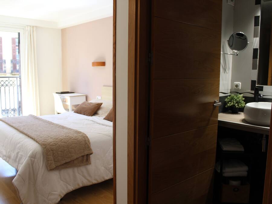 Quarto de hotel com cama, mesa de cabeceira, espelho e banheiro com pia e porta-toalhas.