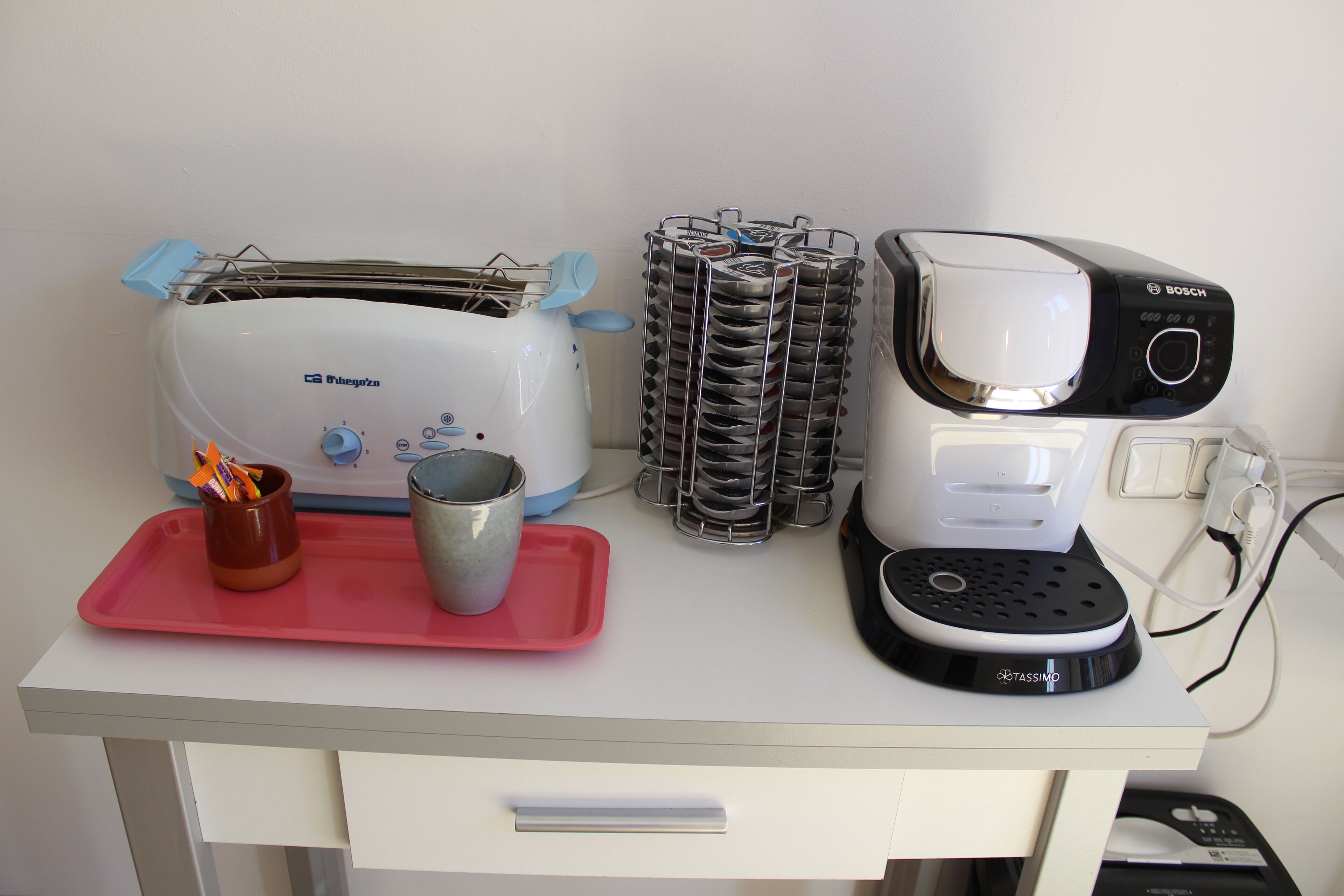 Una encimera de cocina con un tostador, una cafetera y una pila de platos.
