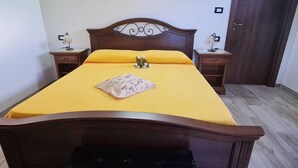 Un lit bien fait, recouvert d’une couvre-lit jaune et agrémenté d’un coussin à motifs floraux, avec deux tables de chevet de chaque côté, sur lesquelles sont posées des lampes.