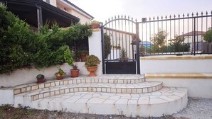Une entrée fermée par un portail, avec un escalier en pierre à volutes menant à un mur blanc.