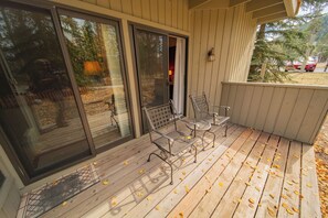 Eine Holzterrasse mit Metallstühlen und einer Bank, überdacht, mit herabgefallenen Blättern auf dem Boden.