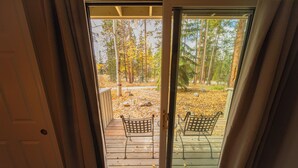 Une terrasse en bois avec deux chaises en métal et une porte vitrée donnant sur une zone boisée.