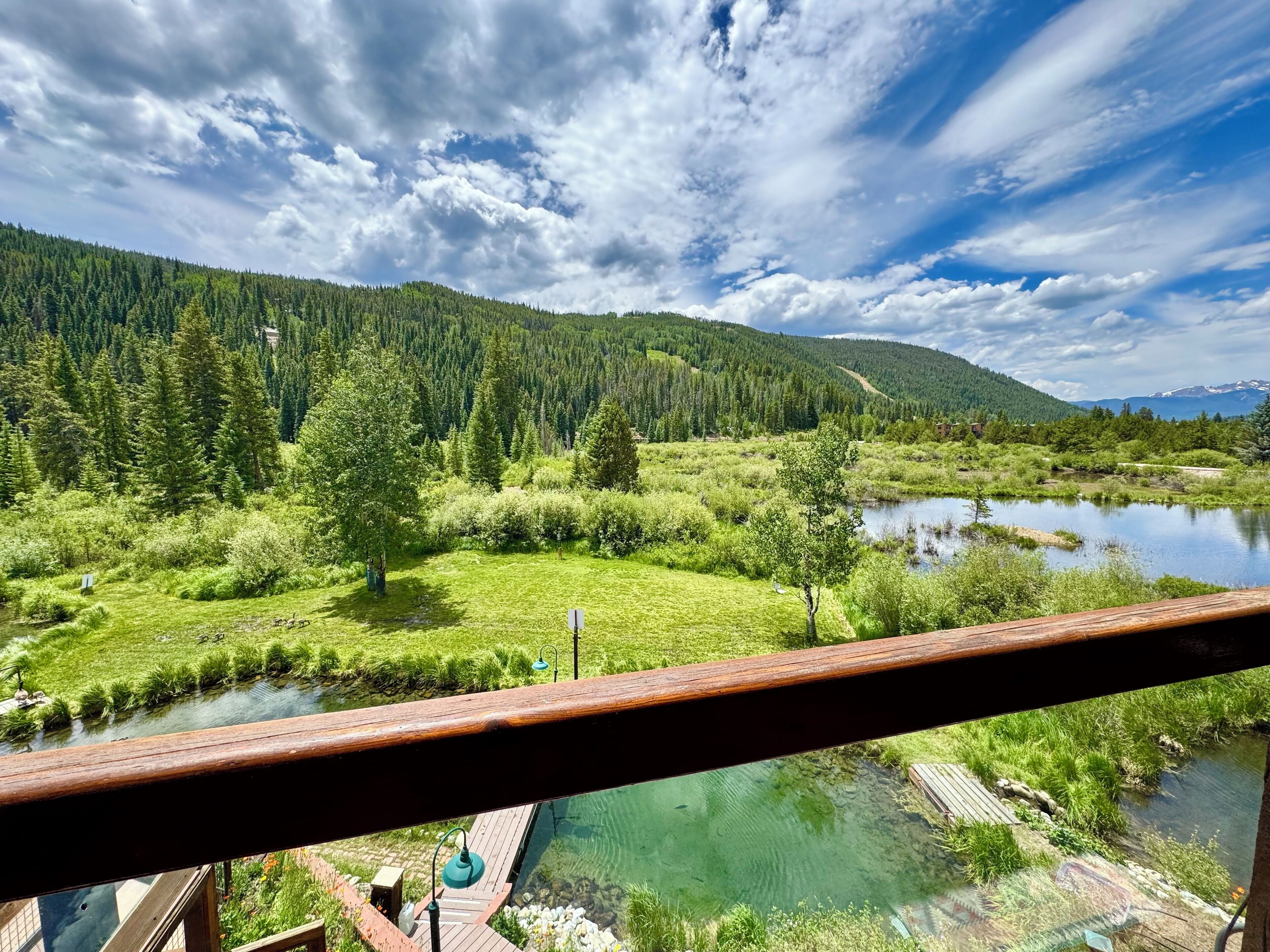 A scenic view from a balcony overlooking a lake, surrounded by lush greenery and mountains.