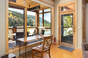 A room with a wooden table and chairs, large windows with a mountain view, and a door with a glass panel. - Mill Creek 201 (Keystone)