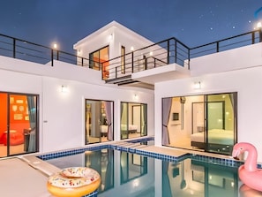 A modern two-story house with a swimming pool, a pink flamingo float, and a balcony.