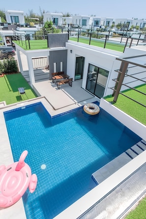 A modern pool area with a clear blue pool, a floating ring, and a pink inflatable toy.
