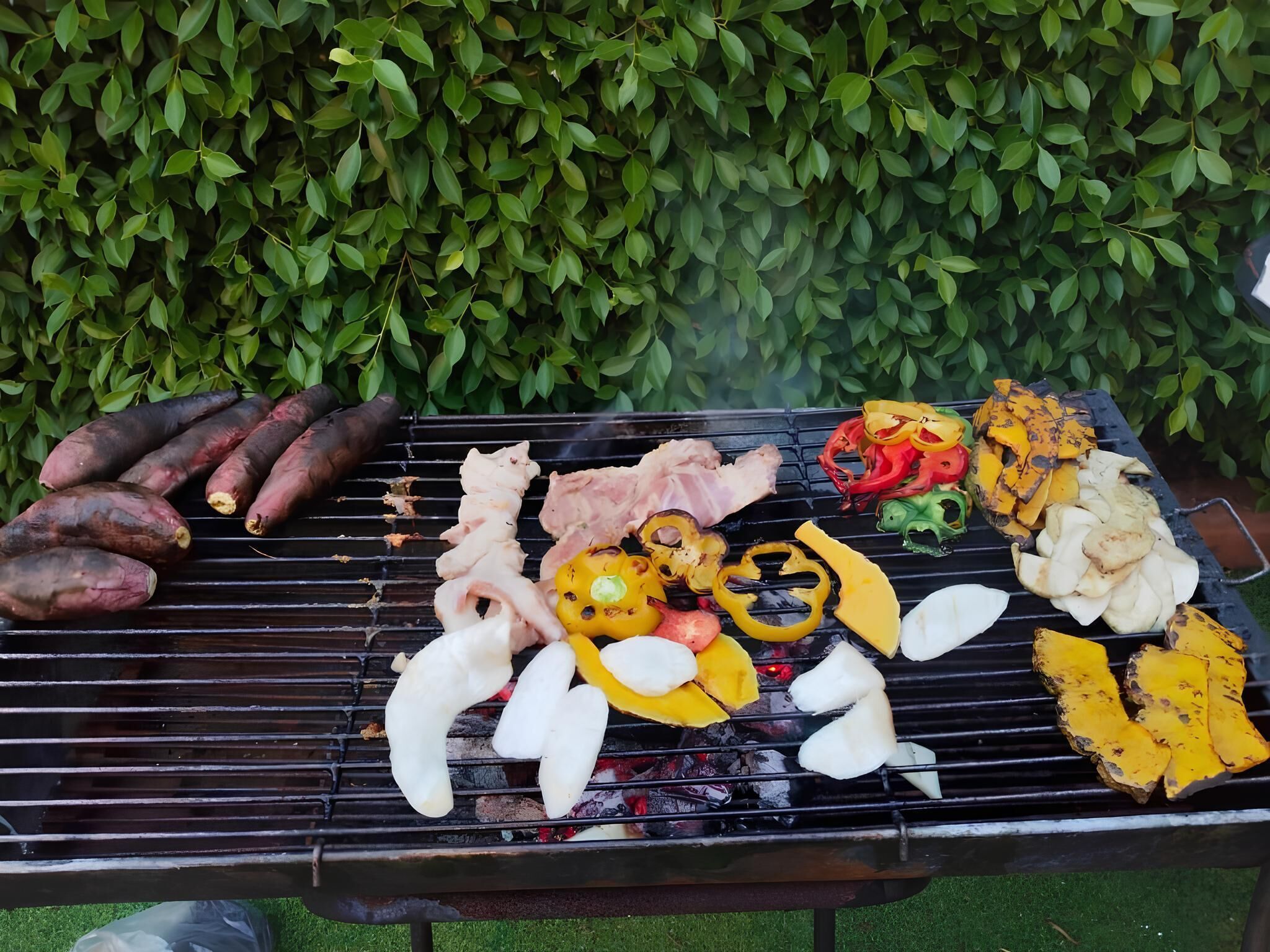 Ein Grill mit verschiedenen Fleischsorten und Gemüse, das zubereitet wird.