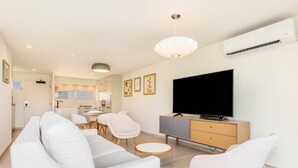 A modern living room with a sofa, chairs, a TV, and a dining area. - 1 Bedroom Suite with Breathtaking Ocean Views! Waikiki Shore 1210 (HONOLULU)