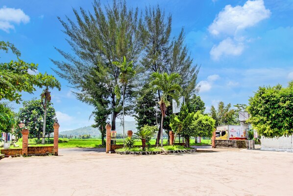 A spacious courtyard with a paved area, surrounded by tall trees and a clear blue sky. - Hotel O Joglo Menoreh Resto & Homestay (Kalirejo)