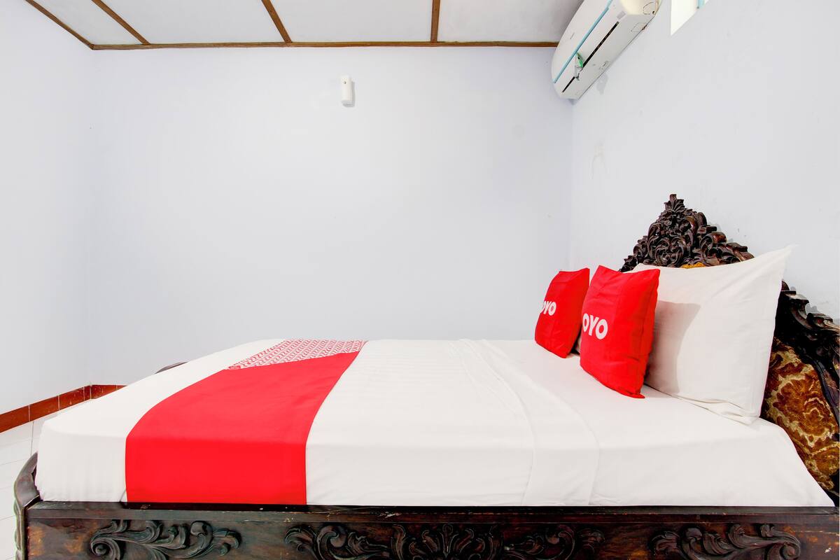 A neatly made bed with a white and red bedspread, two red pillows with "YOYO" text, and a decorative headboard.
