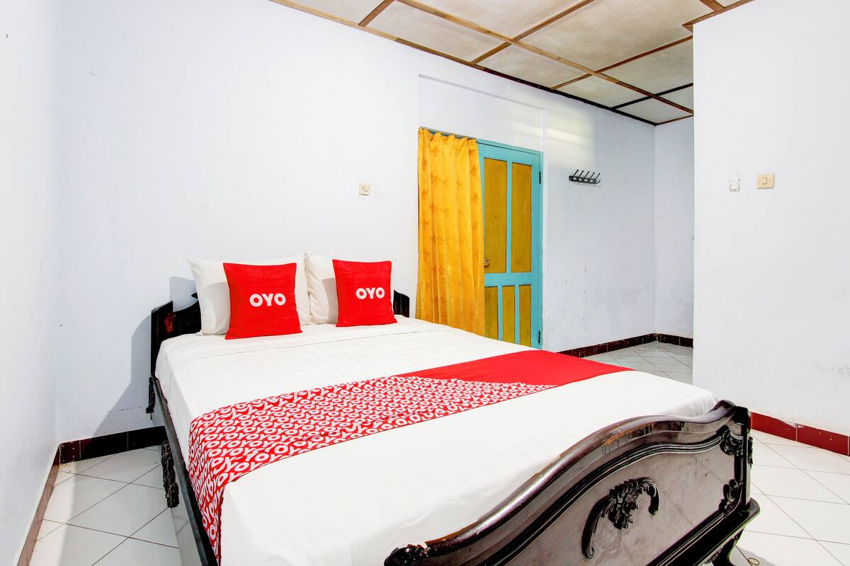 A neatly made bed with red and white bedding, a wooden headboard, and a yellow curtain on a door.