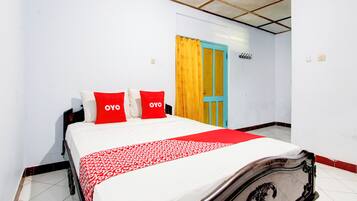 Una cama bien hecha con ropa de cama roja y blanca, un cabecero de madera y una cortina amarilla en una puerta.