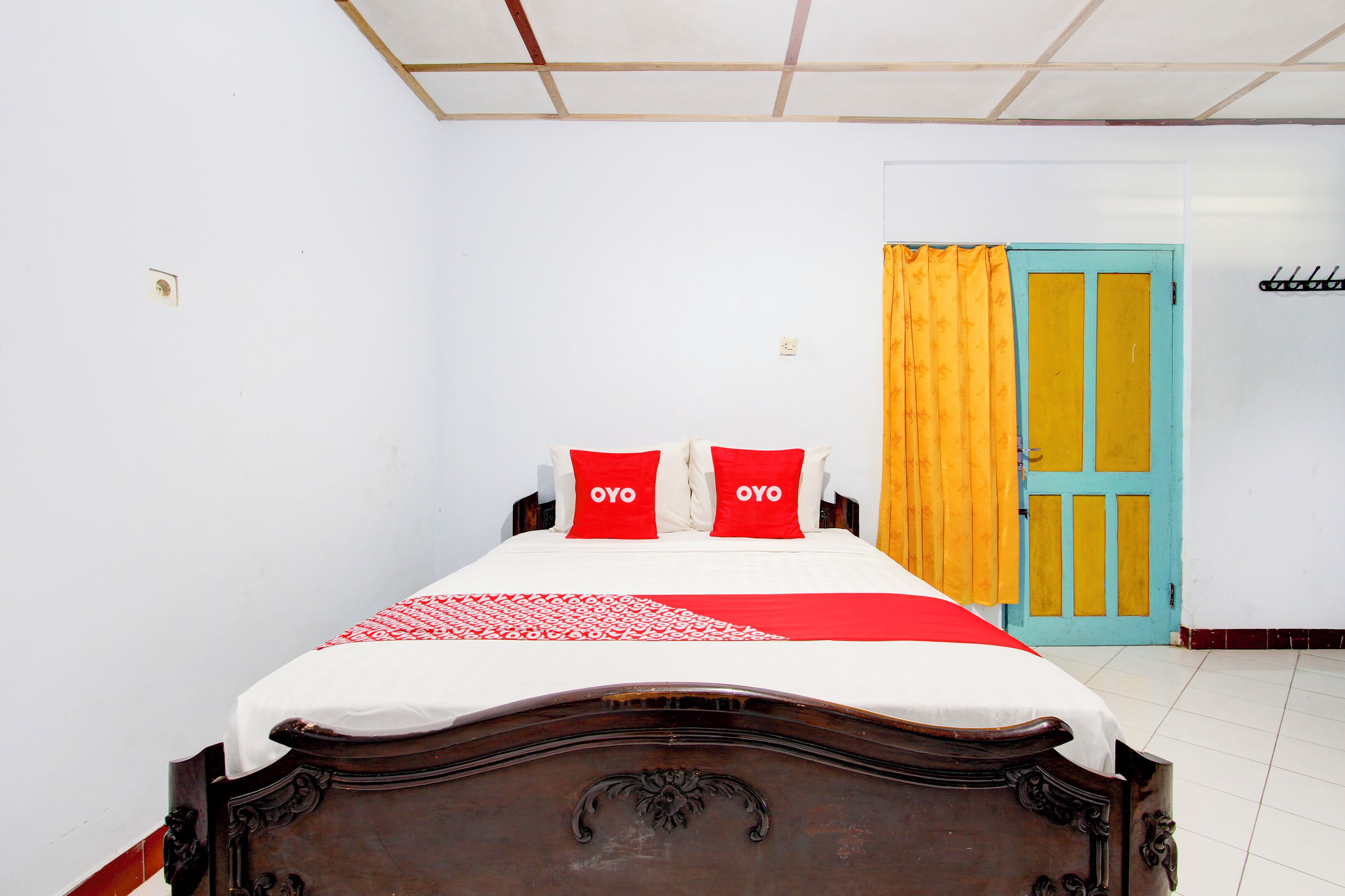 A bedroom with a wooden bed, two red pillows, a white and red bedspread, and a yellow door.