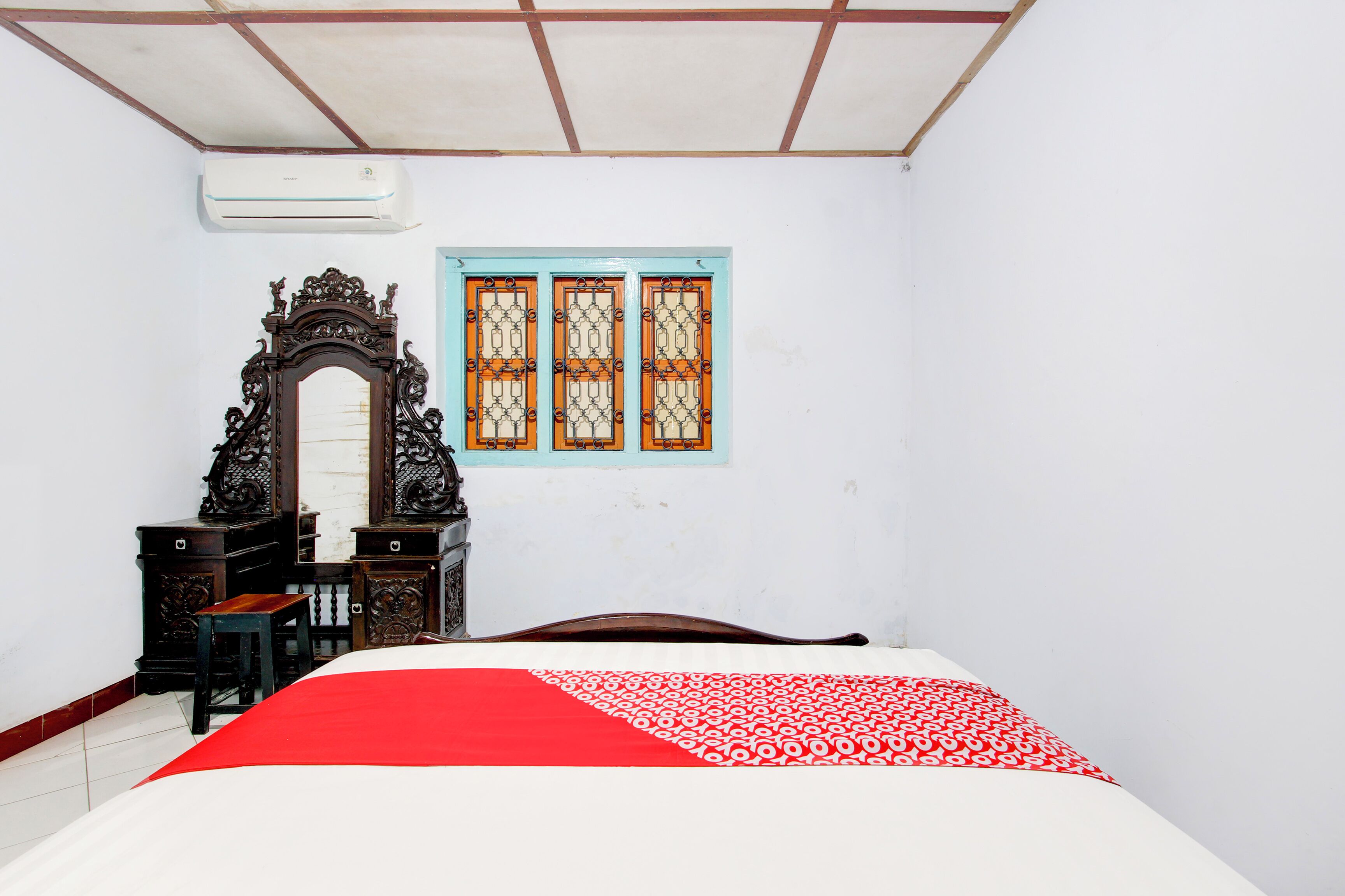 Un dormitorio con una cama, un aparador de madera, un espejo decorativo y una ventana con marco azul.