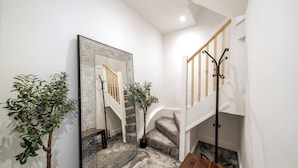 A staircase with a wooden handrail and a black metal railing, flanked by two potted plants and a large mirror with a mosaic frame.