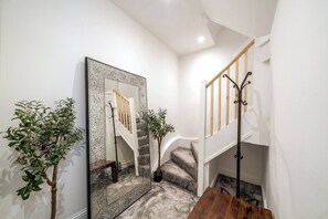 Staircase leads to an upper level, complemented by a large mirror and greenery.