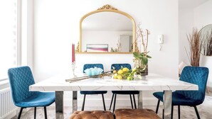 A dining area with a white marble table, blue upholstered chairs, a tufted bench, and a gold-framed mirror above.