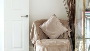 A beige armchair with a cushion, positioned next to a white door and a glass cabinet with decorative items.