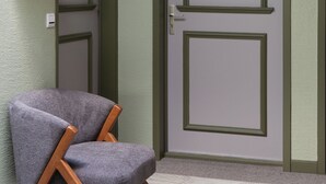 Une pièce avec une porte portant les inscriptions « 5 » et « Trans », un fauteuil à revêtement gris et une étagère en bois adossée au mur.