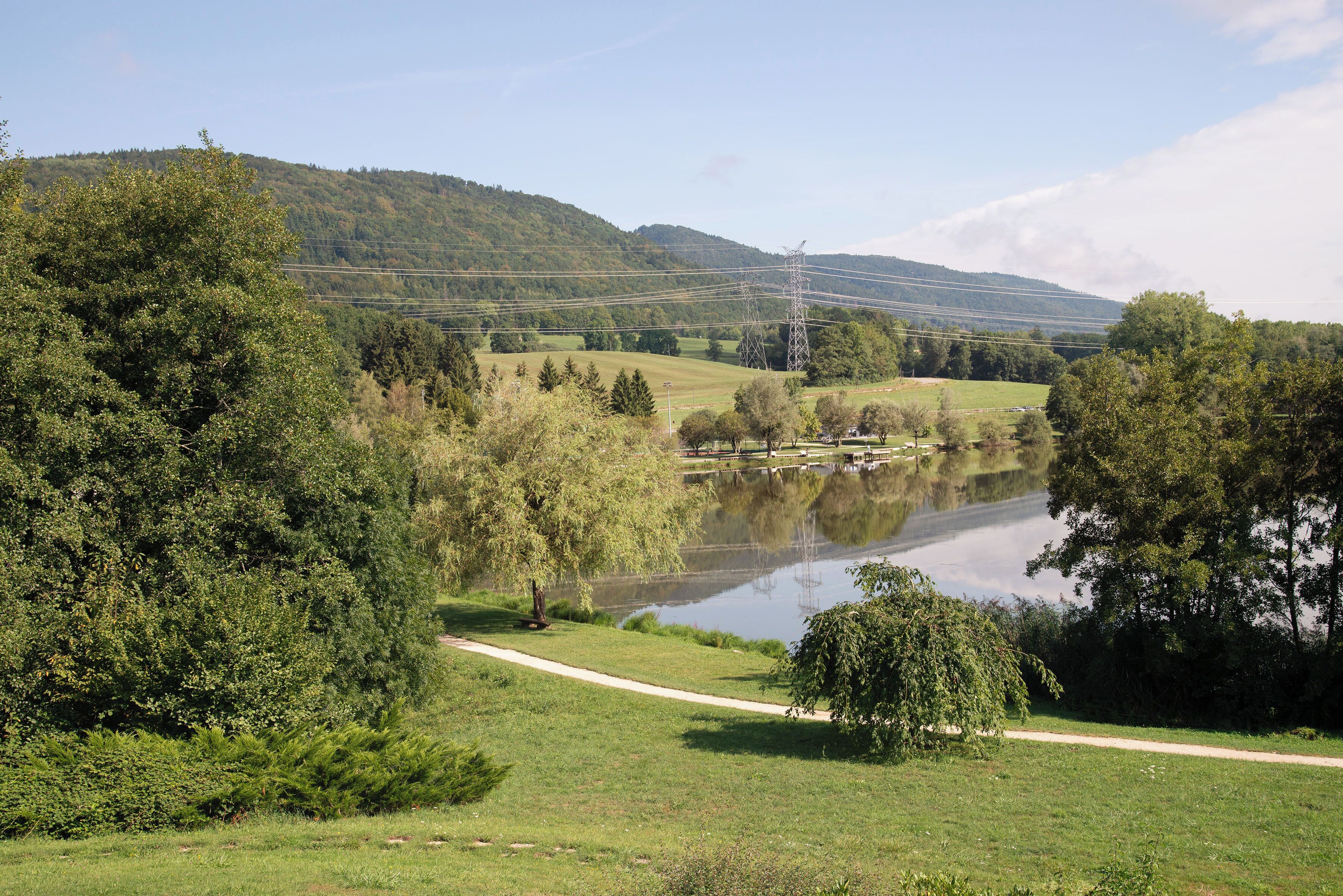 A serene landscape with a lake, pathways, and a hill in the background.