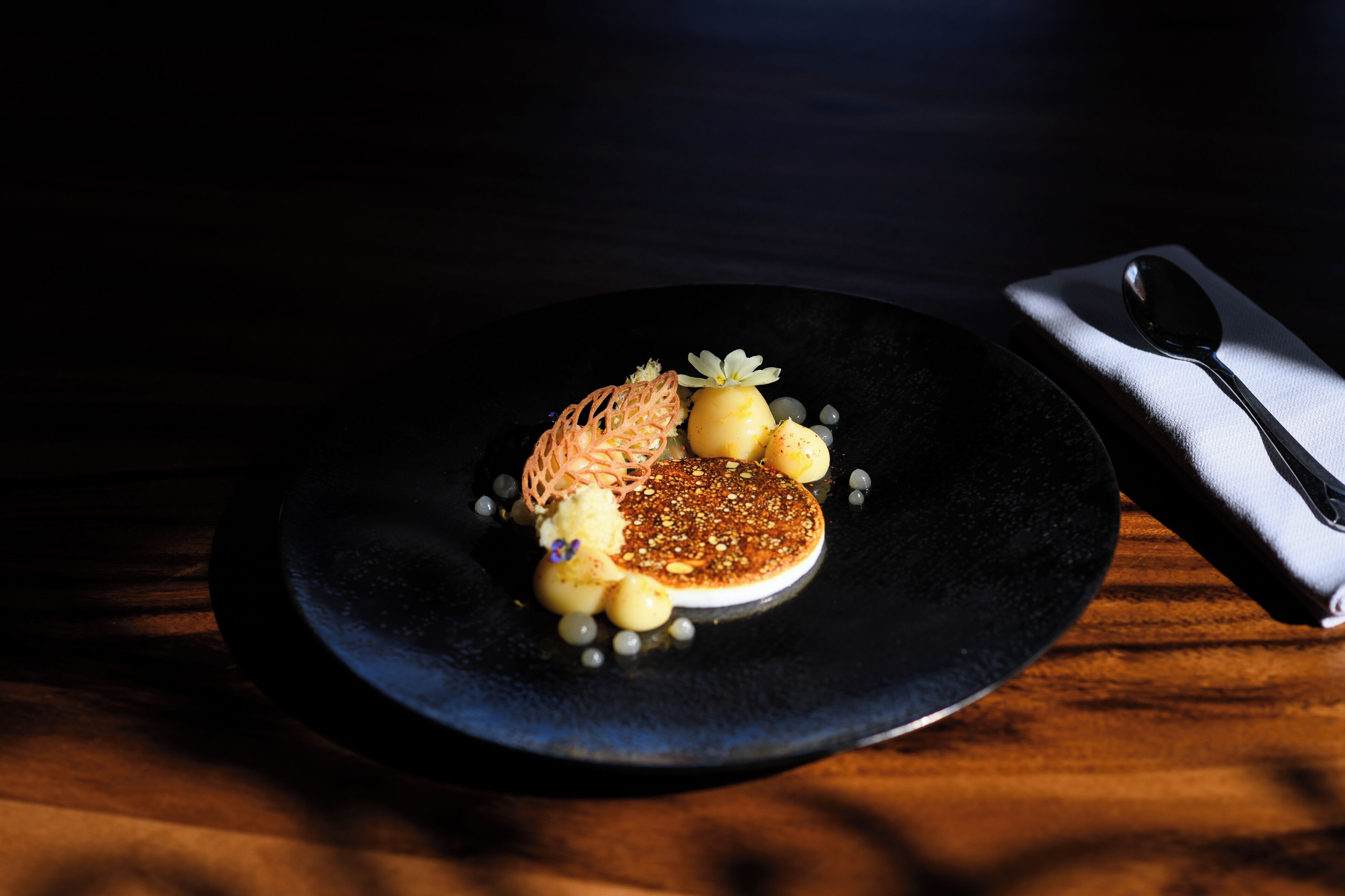 Un plato negro con un postre sobre una mesa de madera.