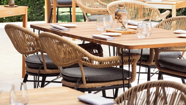 Un espace extérieur aménagé pour les repas, avec des meubles et des tables en osier, prêts pour un repas.