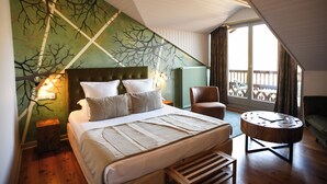 Une chambre avec un grand lit, une table de chevet en bois, une chaise et une vue sur l’extérieur grâce à un balcon.