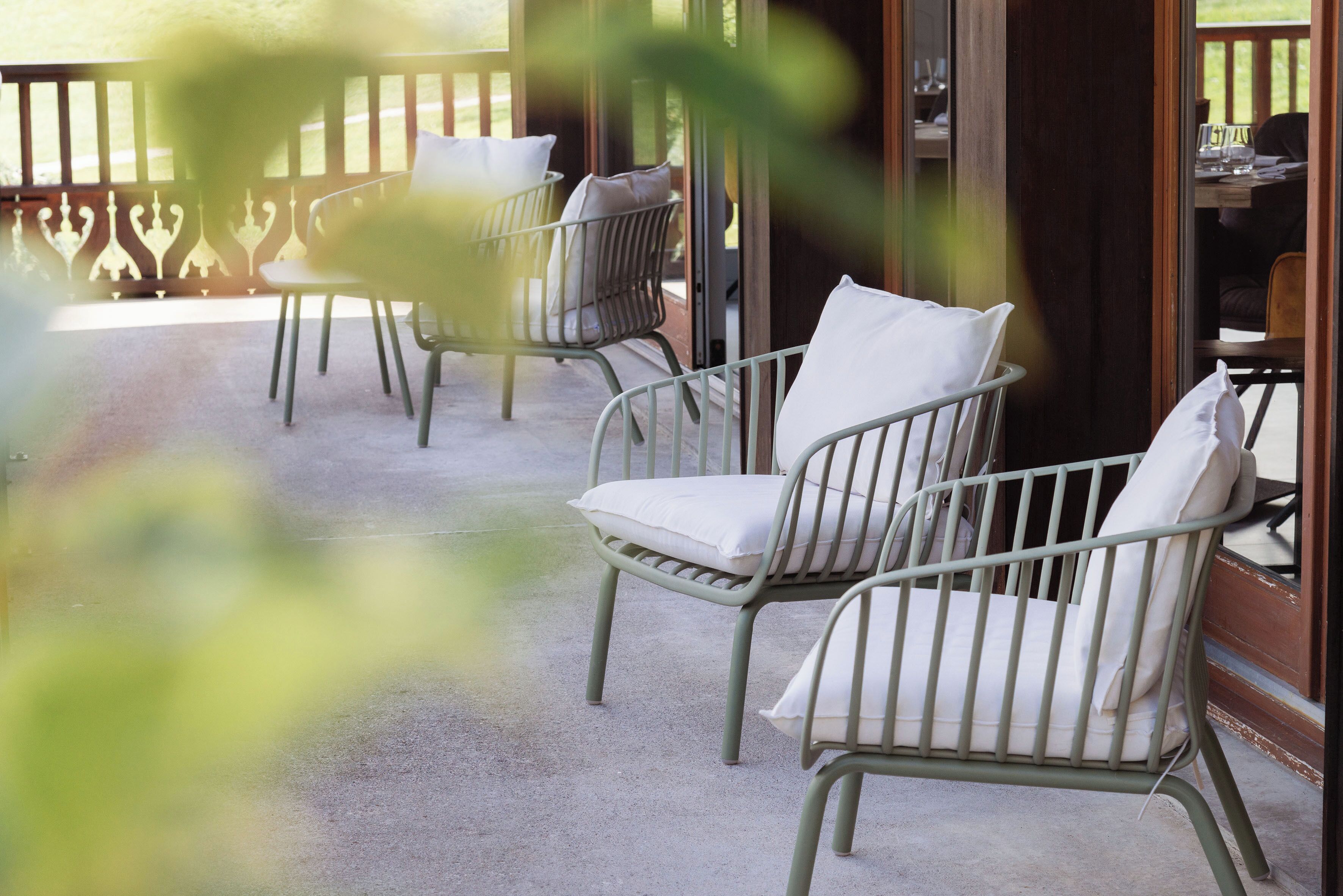 A covered patio area with metal chairs and cushions, a wooden deck railing, and a table with chairs.
