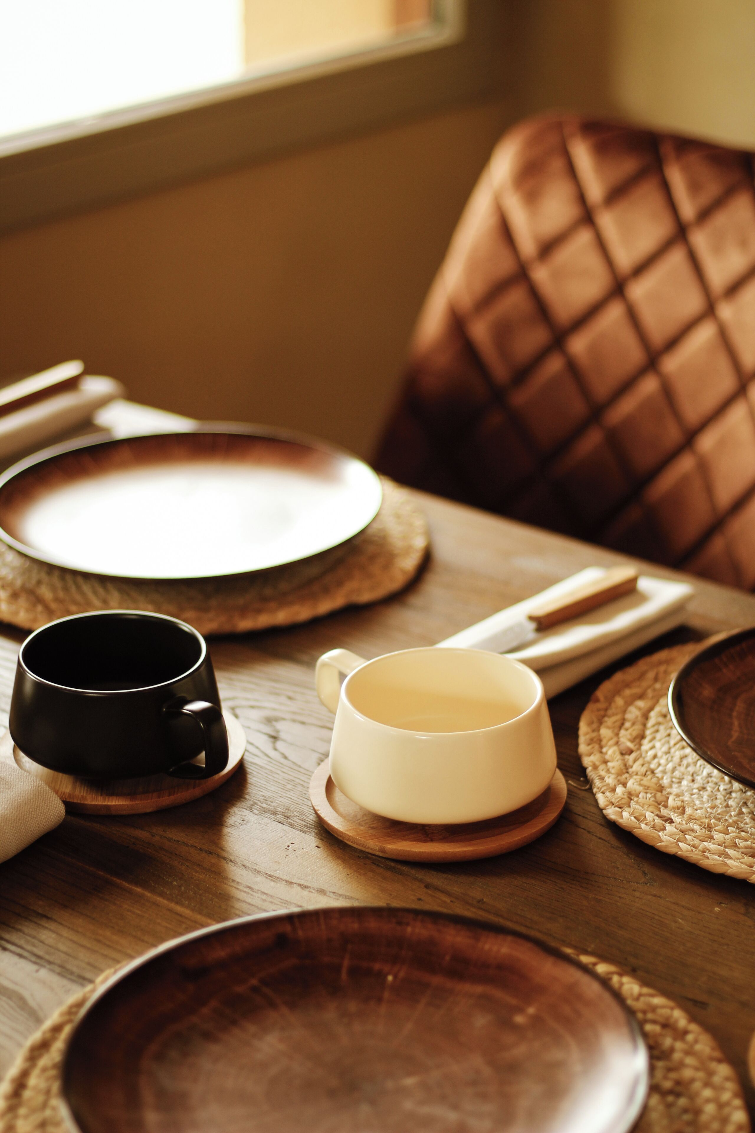 Ein Esstisch mit Holzschalen, einer schwarzen Tasse und einer weißen Tasse, auf gewebten Platzsetszen.