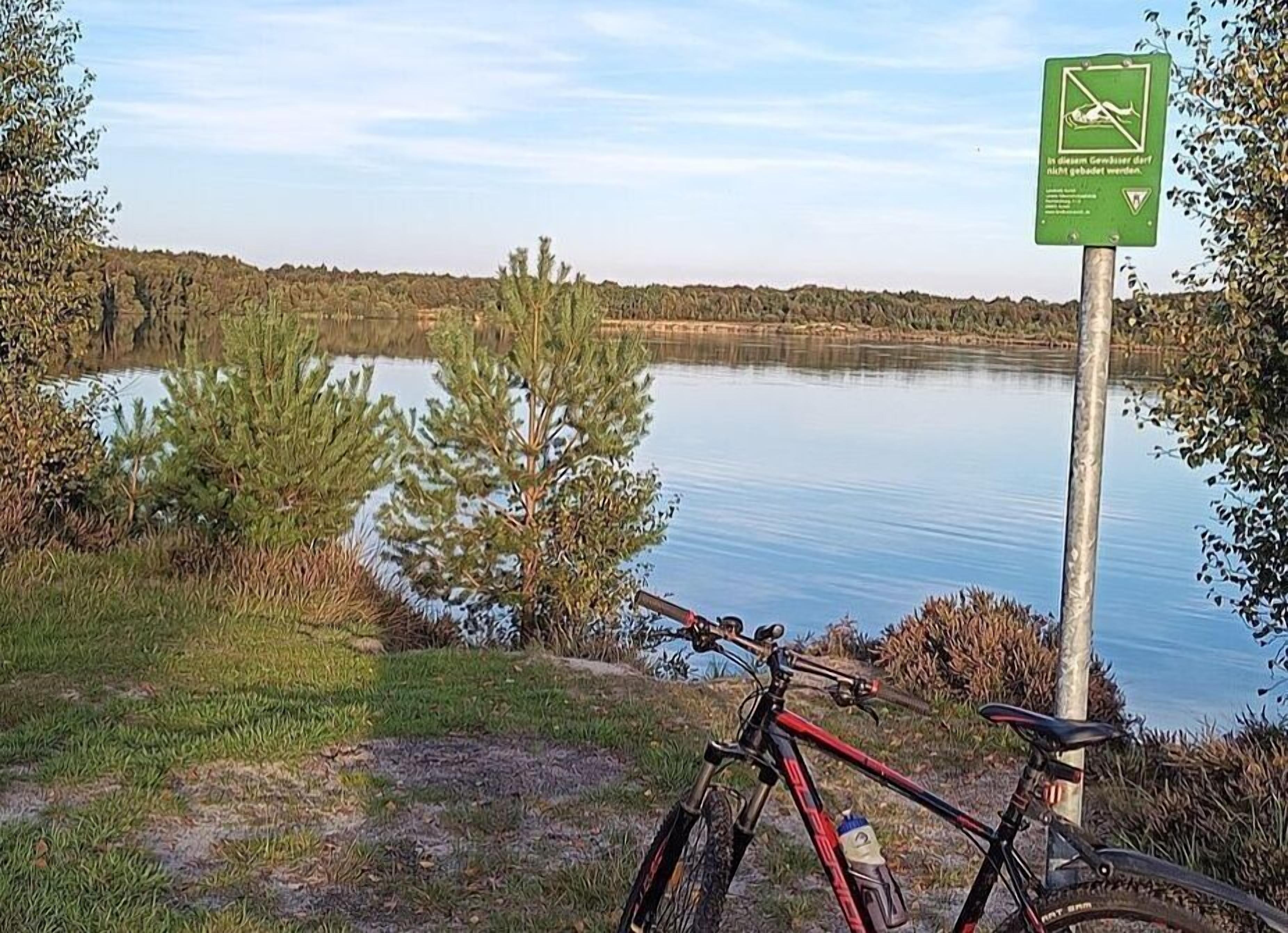 A mountain bike parked by a lake with a sign indicating no camping.
