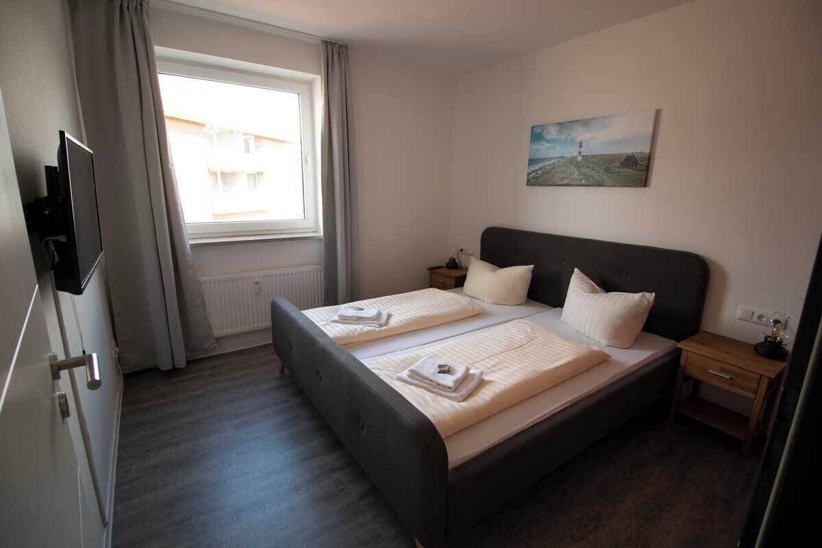 A bedroom with two beds, a TV, a painting, and a window with curtains.