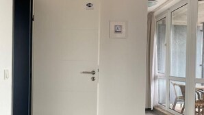 A modern living room with a grey sofa, a white door with a Wi-Fi symbol, and a large window with a view of the outdoors. - Hafen Apartments  (Aurich)