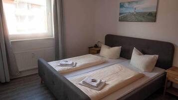 A bedroom with a large bed, two bedside tables, a window with curtains, and a painting on the wall.