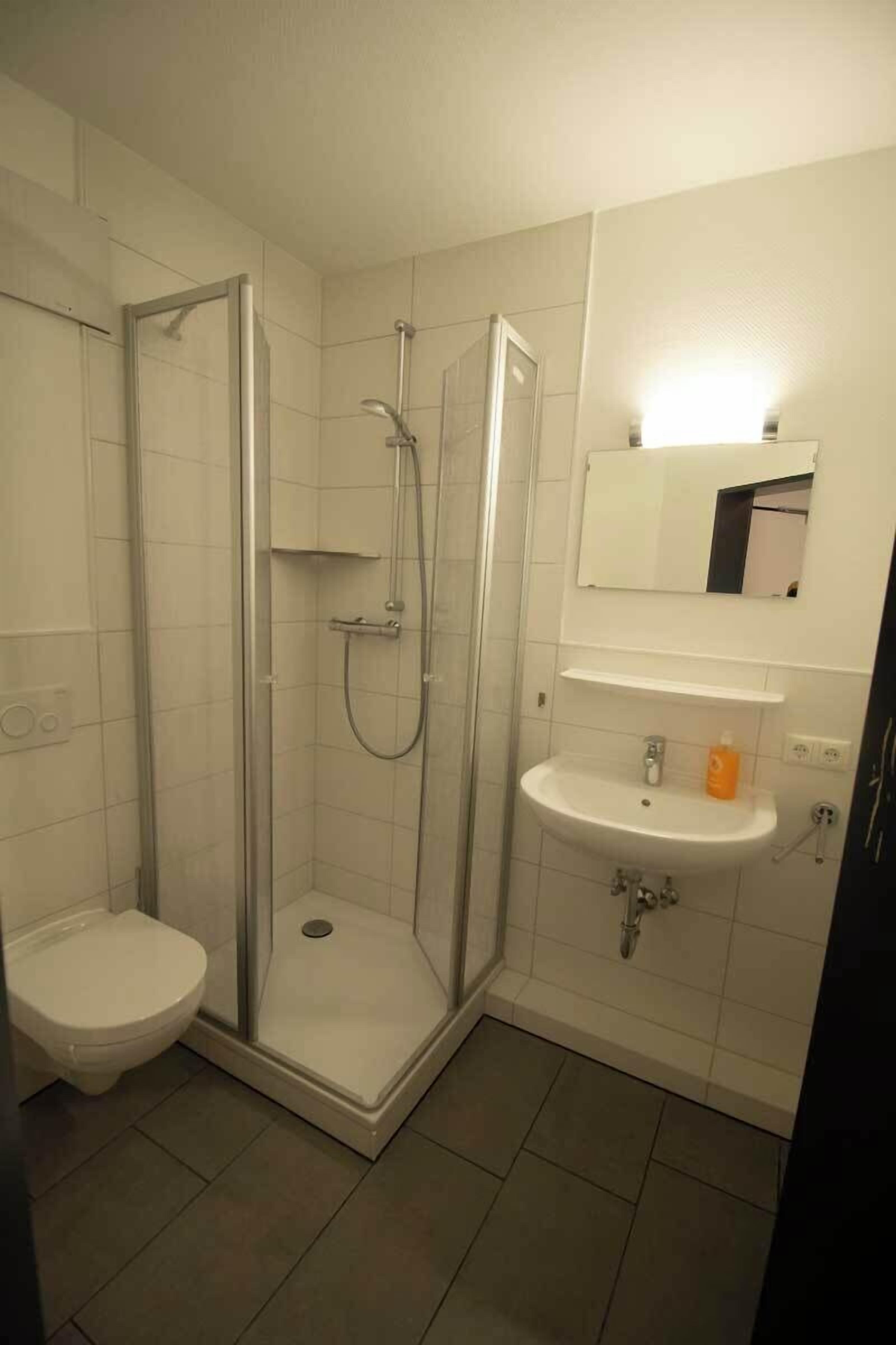 Un baño con ducha envuelta en vidrio, un lavamanos blanco y un inodoro.