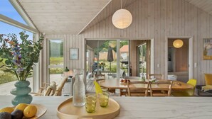 Un intérieur moderne avec un plafond en bois, un coin repas comprenant une table et des chaises, une grande fenêtre et une vue sur l’extérieur.