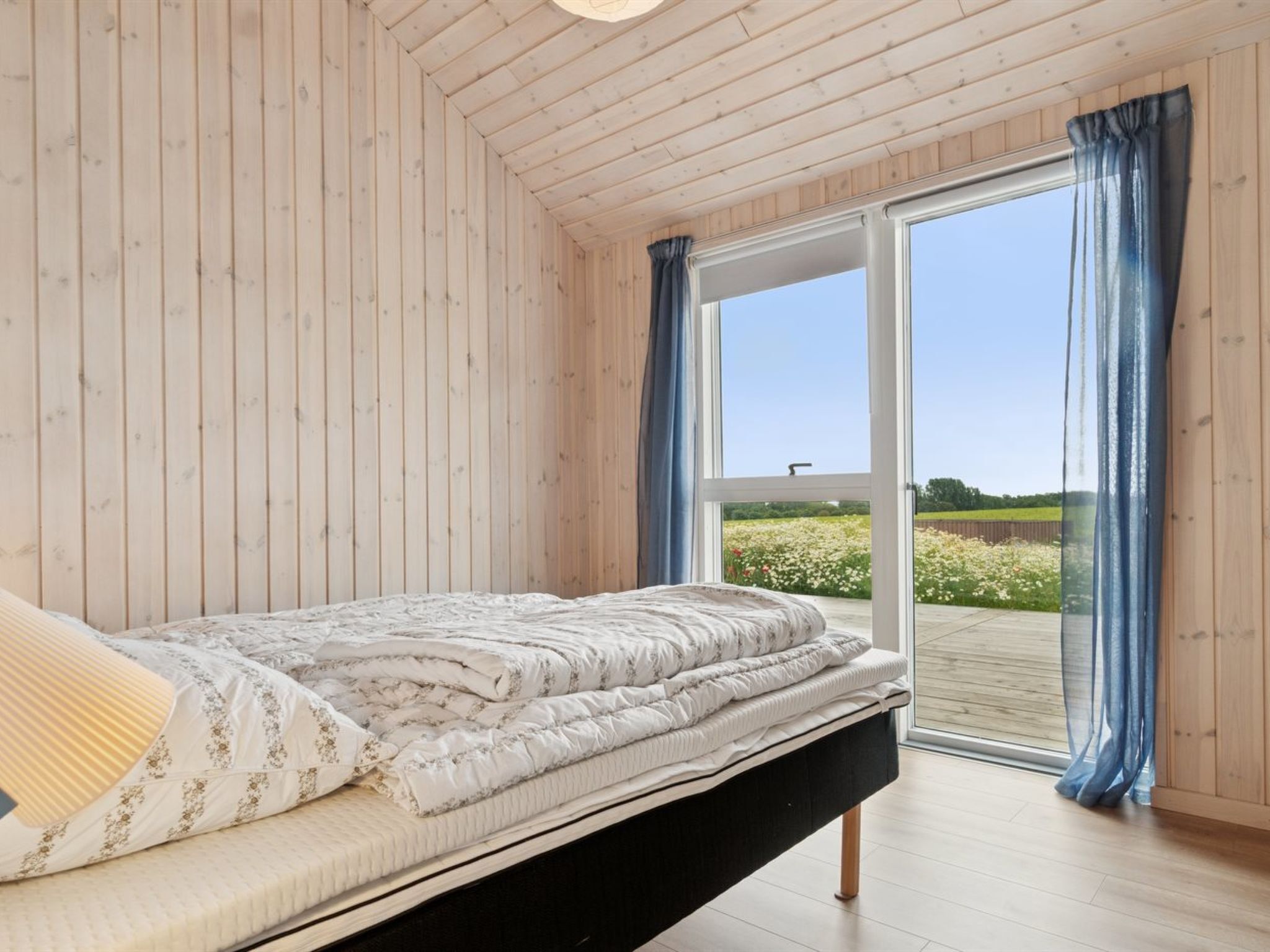 A bedroom with a bed, wooden walls, and a large sliding glass door leading to an outdoor area.