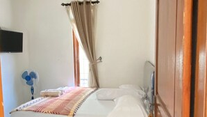 A bedroom with a bed, an air conditioning unit, a fan, and a window with curtains. - ZG Home Solo (Surakarta)