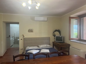 A bedroom with a bed, a television, a window, and a bathroom visible in the background.