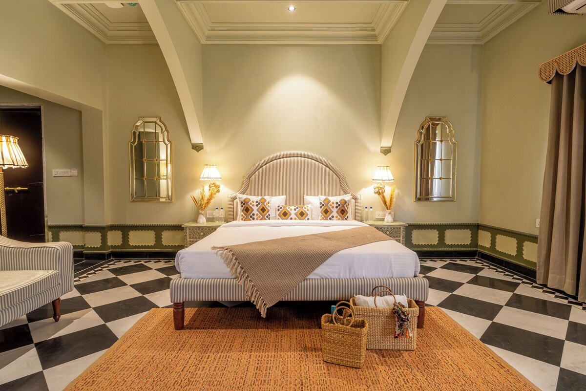 A hotel room with a large bed, two bedside tables with lamps, a checkered floor, and a patterned rug.
