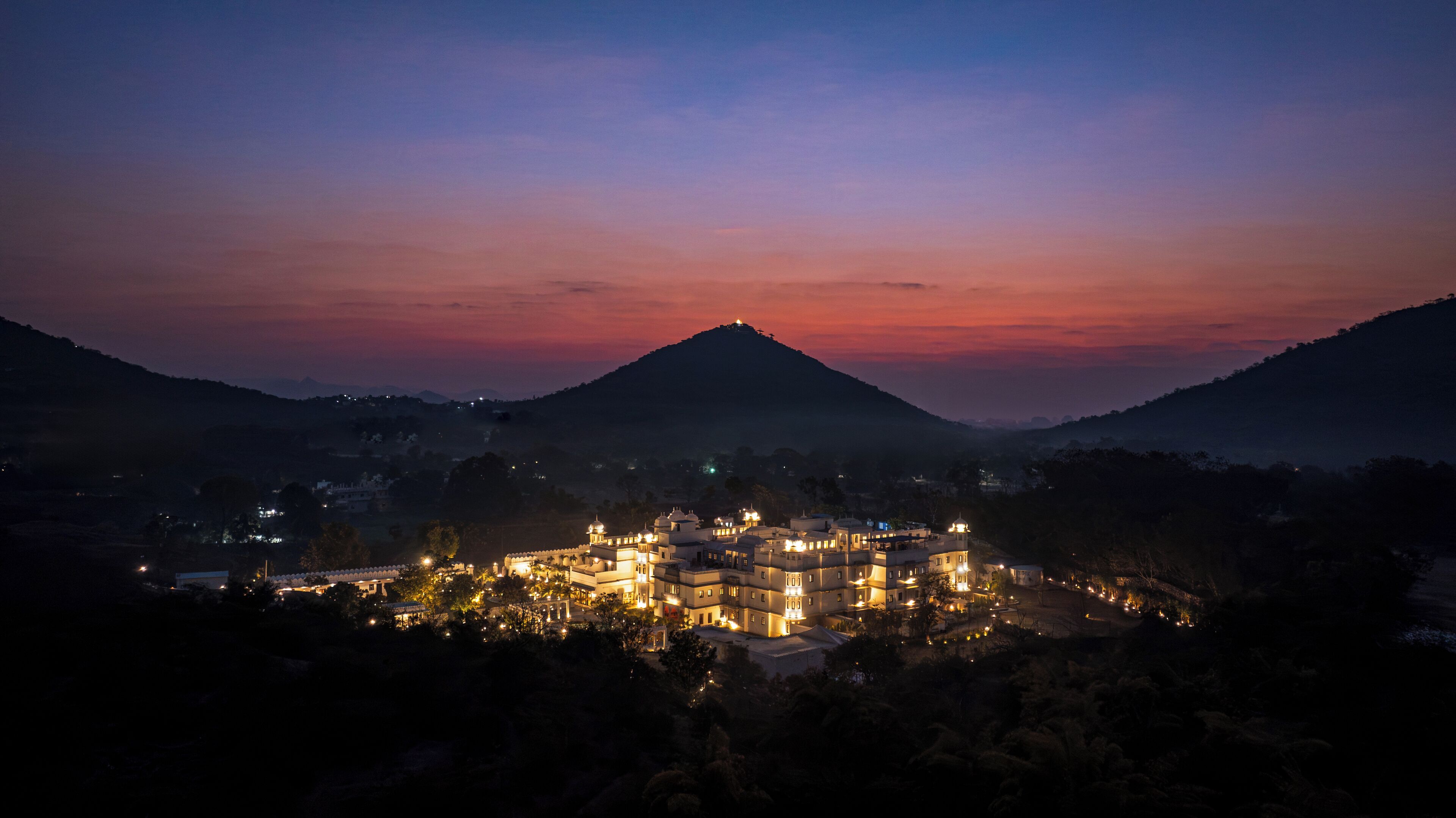 Ein gut beleuchtetes Resort mit mehreren Gebäuden, umgeben von Hügeln und einem Berg im Hintergrund.