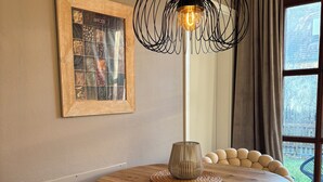 A dining area with a round wooden table, cushioned chairs, a woven placemat, a pendant light, and a framed picture on the wall.