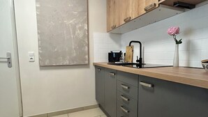 A modern kitchen with a wooden countertop, grey cabinets, a white tiled backsplash, and a large abstract painting on the wall.