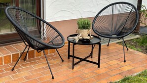 Two black wireframe chairs on a tiled patio with a small table and a potted plant.