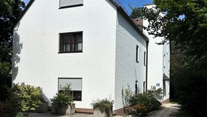 A white building with a gabled roof, a paved driveway, and potted plants.