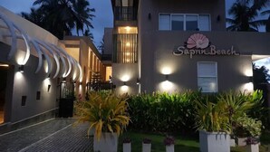 L’entrée d’un hôtel, agrémentée d’une enseigne indiquant « Sapna Beach », présente un design moderne avec un balcon et un escalier menant à l’entrée.