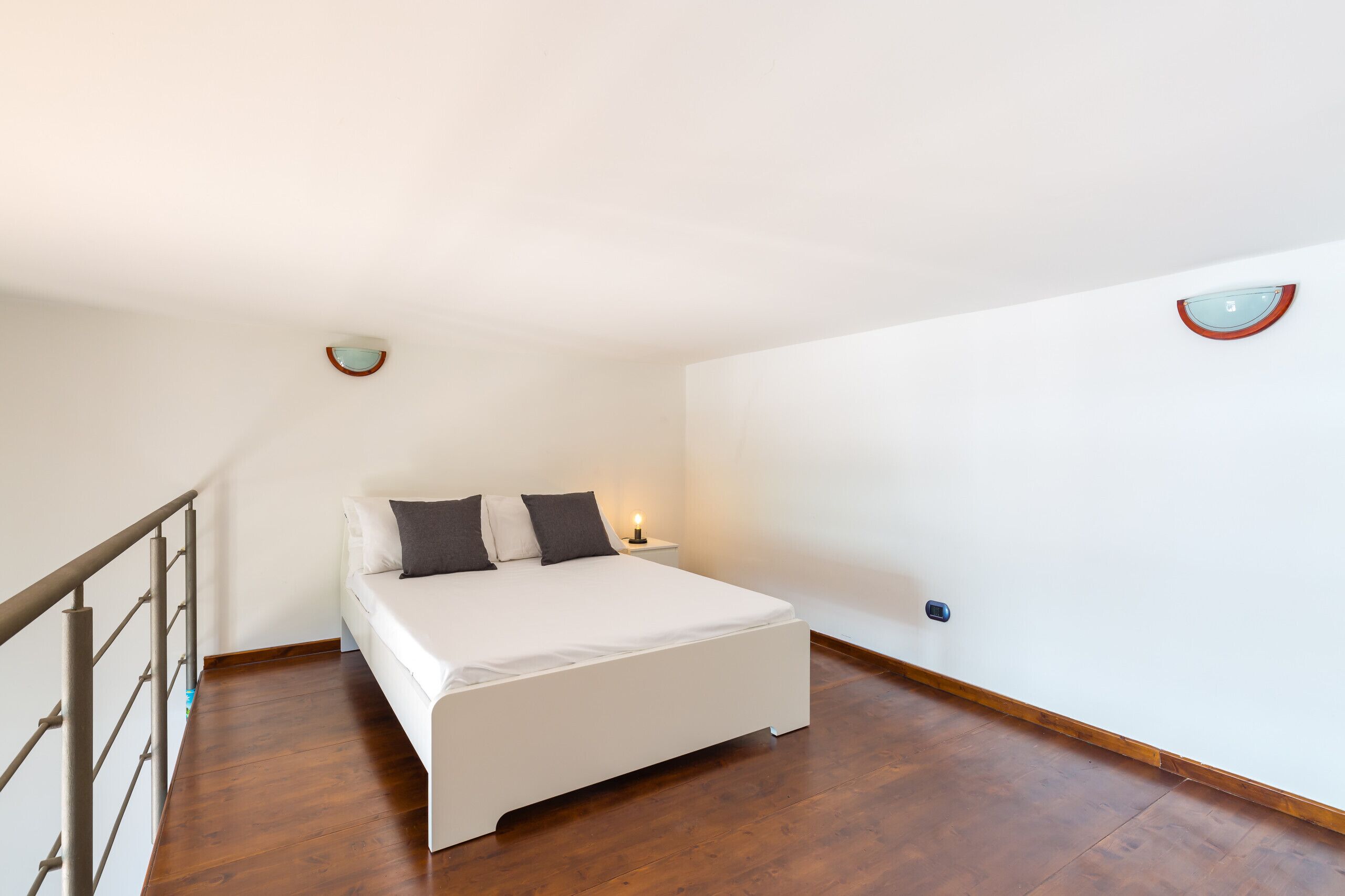 A bedroom with a bed, a nightstand, and a wall-mounted light fixture.