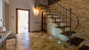 A spacious room with a spiral staircase against a textured wall, a bench, and a door leading outside. - Partenope Spacious Home (Naples)