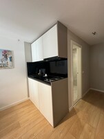 Una cocina compacta con armarios blancos, encimera negra y suelo de madera.