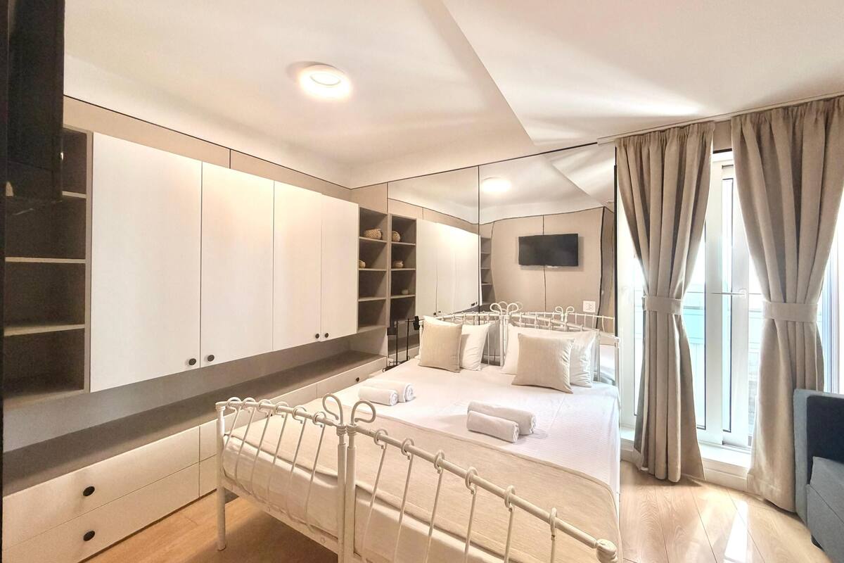 A bedroom with a bed, a wardrobe, a TV, and a window with curtains.