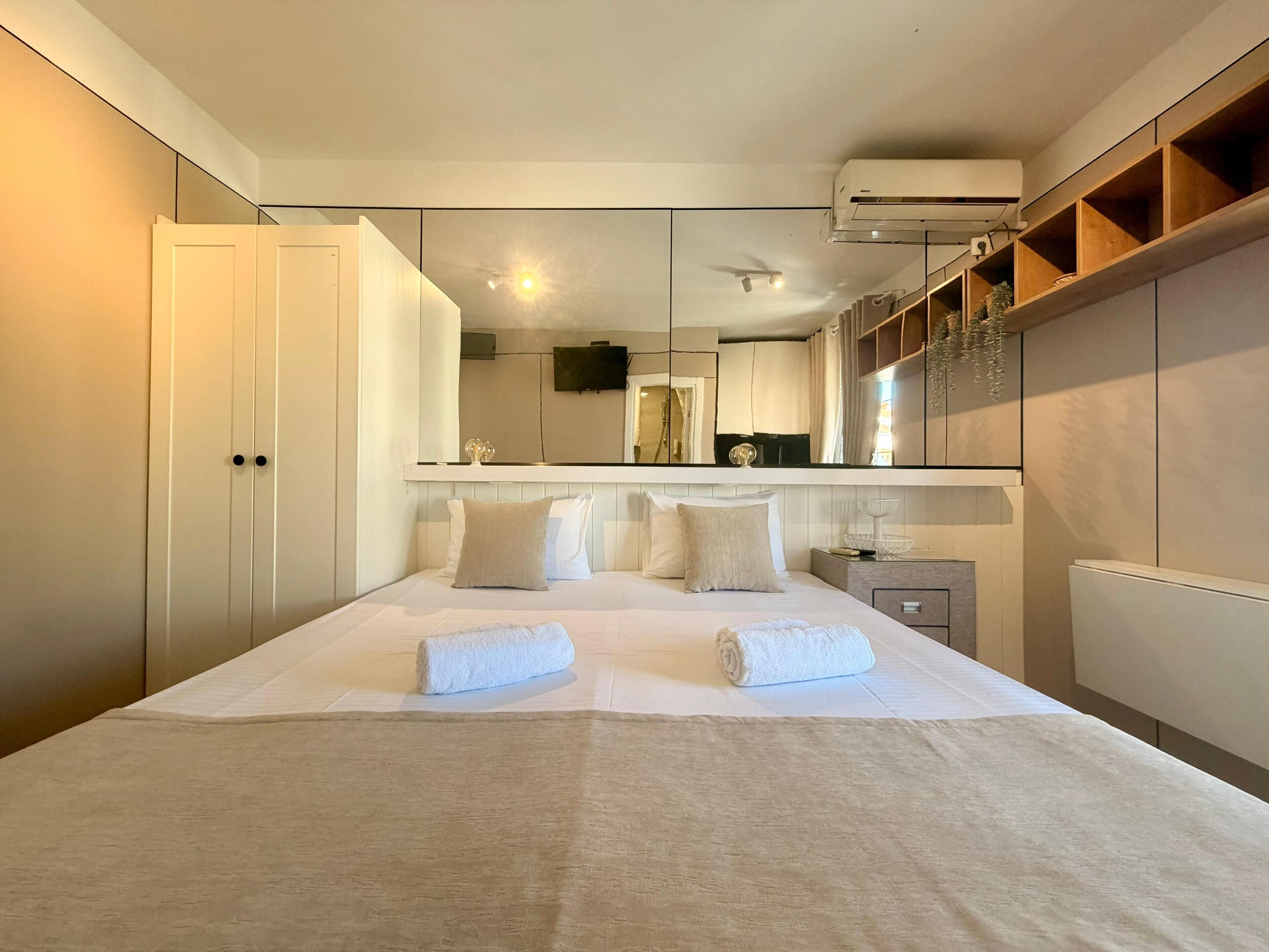 A bedroom with a large bed, a mirror, a wardrobe, and an air conditioning unit.